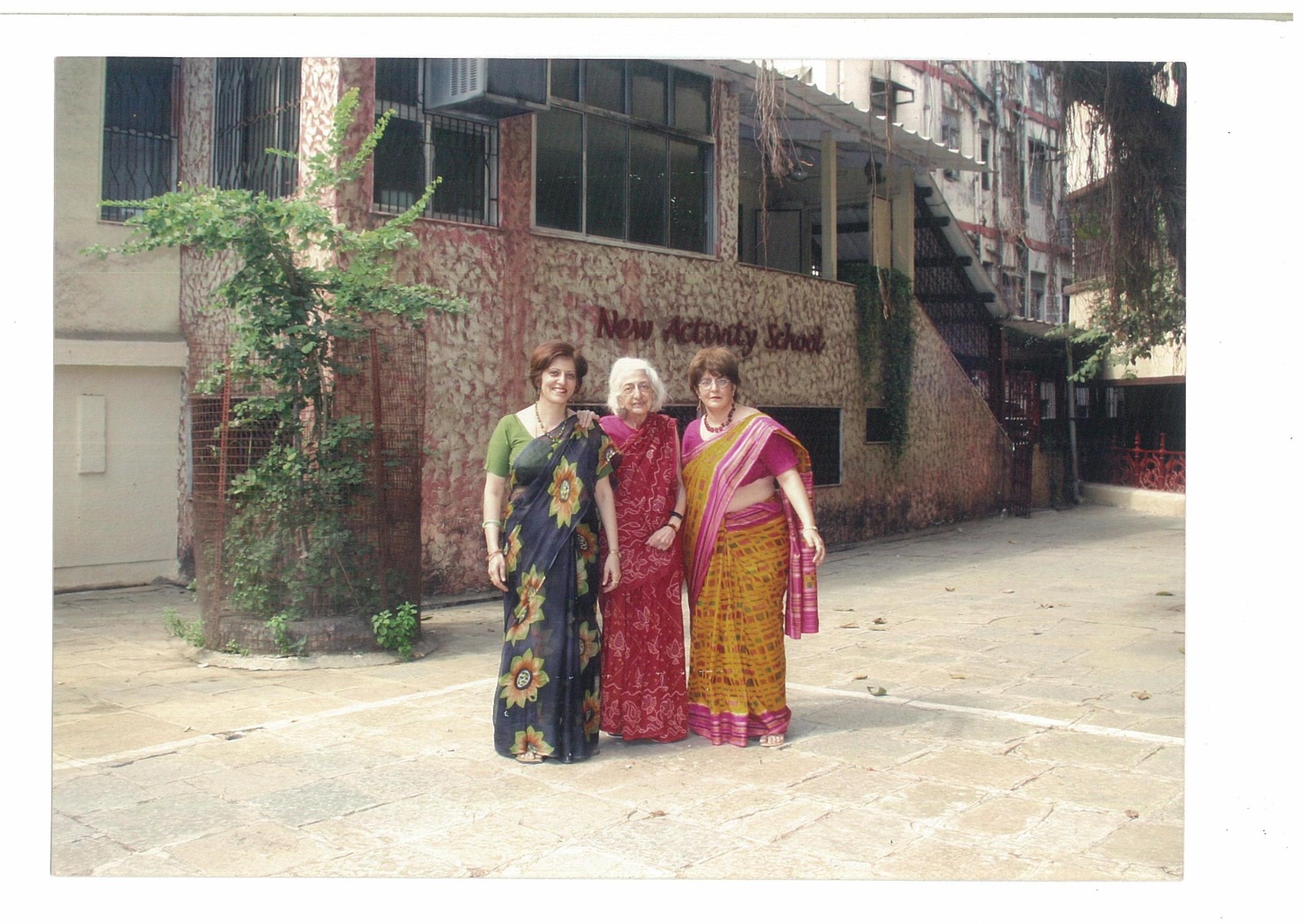 Three women standing together in the NAS courtyard near the New Activity School building